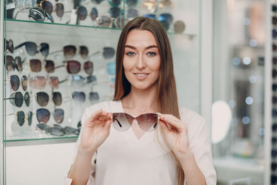 Portrait of smiling woman holding sunglasses at store