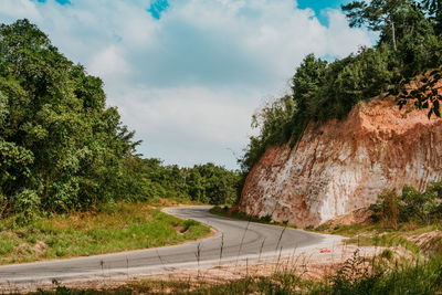 Road amidst trees and hill against sky