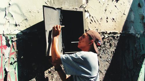 Young man writing on metallic door mounted over weathered wall