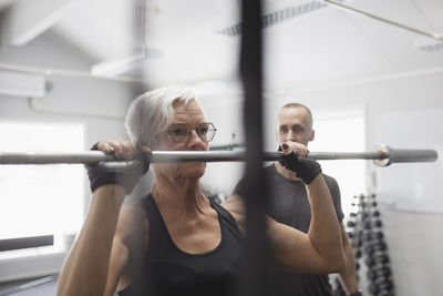 Senior woman lifting barbell pole in gym