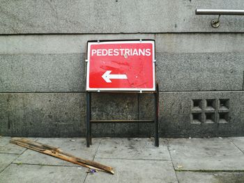 Pedestrian crossing sign on footpath against wall