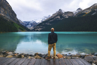 Rear view of man standing on jetty looking at lake and mountains
