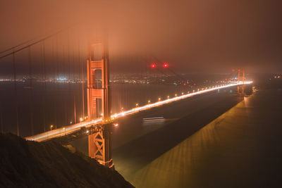 Illuminated bridge over river in city against sky at night