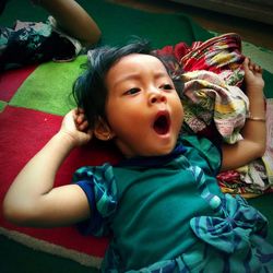 High angle view of cute baby girl yawning while lying on bed at home