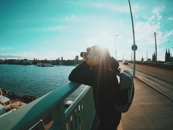 Man photographing while standing on footpath by street against sky