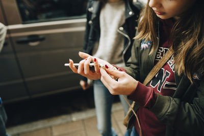 Midsection of girl connecting cable to mobile phone while walking with friends