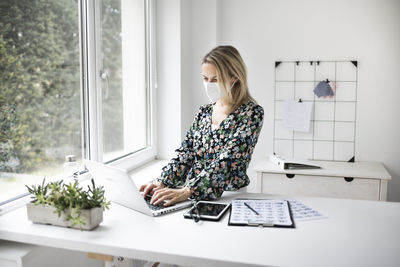 Businesswoman wearing mask using laptop at home