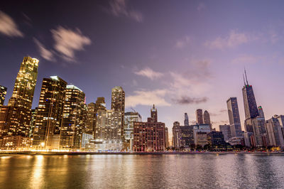 Illuminated buildings by river against sky at night