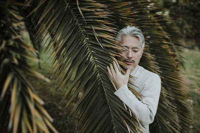 Mature man with gray hair touching palm leaves