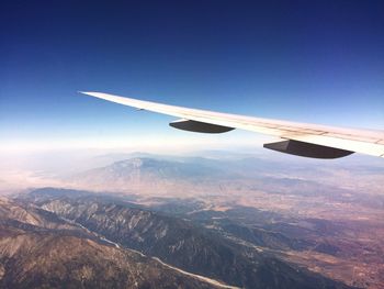 Aerial view of airplane wing over landscape against blue sky