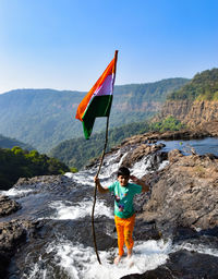 Boy standing on rock by mountain against sky with indian flag