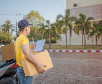 Delivery man with package reading clipboard while standing on street