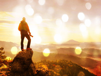 Rear view of woman standing on rock at sunset