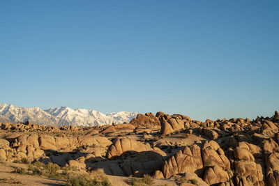 Scenic view of snowy mountains behind desert rock against clear blue sky