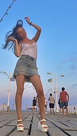 Full length of woman with arms raised in city against blue sky