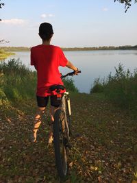 Rear view of boy standing on field by lake against sky