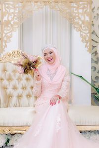 Bride in hijab holding bouquet while sitting on sofa