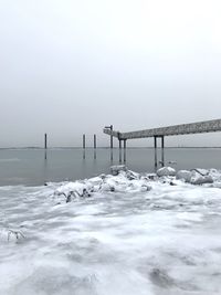 Snow covered land by sea against clear sky during winter