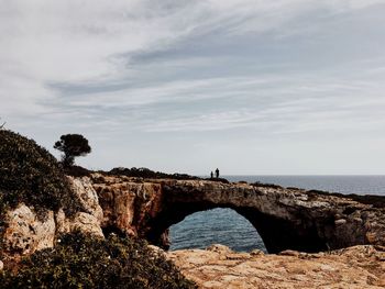 Man standing on cliff by sea against sky