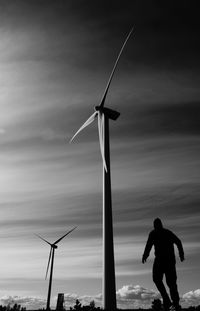 Silhouette man standing on wind turbines against sky