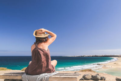 Woman sitting on bench at beach against clear sky