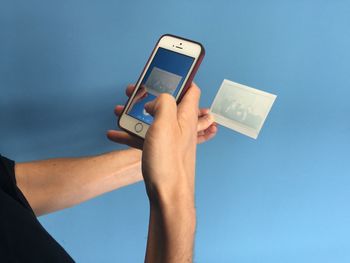 Cropped image of person photographing of photograph with smart phone against blue background