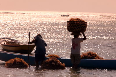 Worker carrying whicker basket by boat in sea on sunny day