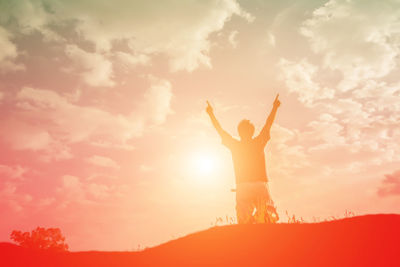 Silhouette woman with arms outstretched standing against sky during sunset