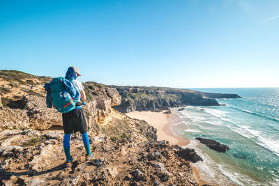 Rear view of man standing on beach against clear blue sky