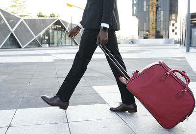 Side view of african american male entrepreneur wearing classy suit walking with suitcase towards airport for departure
