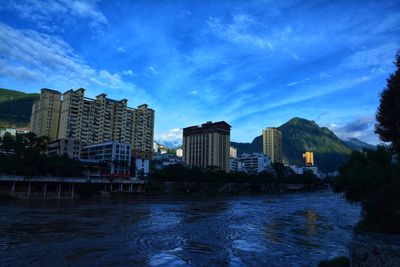 Buildings by river against blue sky