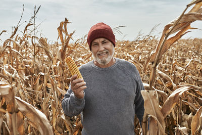 Smiling farmer holding corn while standing at farm