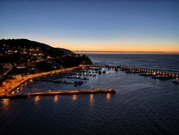 Illuminated city by sea against clear sky at sunset