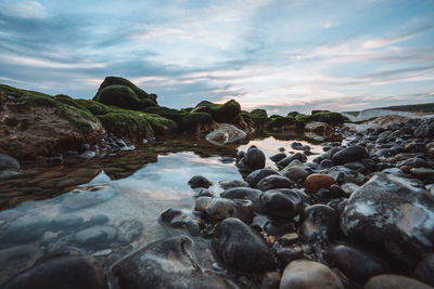 Rocks on beach against sky during sunset