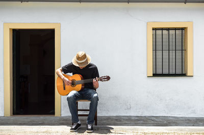 Full length of mn playing guitar while sitting on chair at entrance