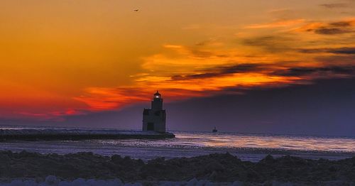 Lighthouse by sea against sky during sunset