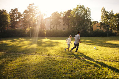 Full length of father and son playing soccer on grassy field during sunny day