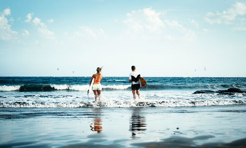 Rear view of men on beach against sky