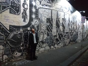 Man standing by graffiti on wall in city
