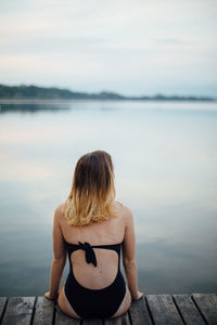 Rear view of woman sitting on pier over river against sky