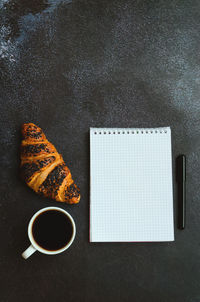 Businessman working morning with notebook, cup of hot coffee and sweet croissant on black background