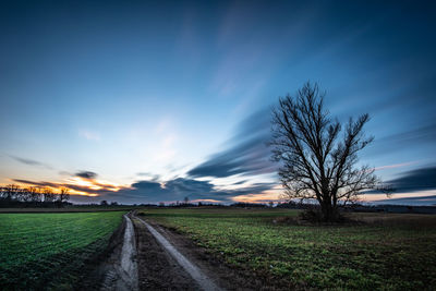 Empty road amidst field against sky at sunset