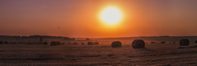 Hay bales on field against sky during sunset