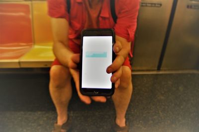 Midsection of man using mobile phone in train