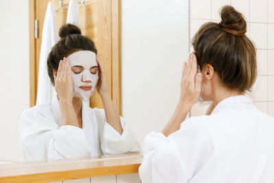 Woman with eyes closed applying sheet mask