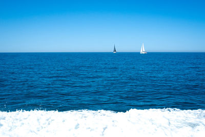 Sailboat sailing in sea against clear blue sky