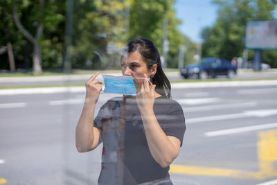 Young woman using phone while standing on road in city