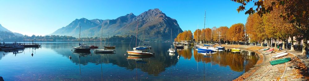 Panoramic view of boats moored in lake with reflections against mountains