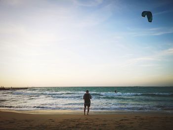 Rear view of man standing on beach against sky