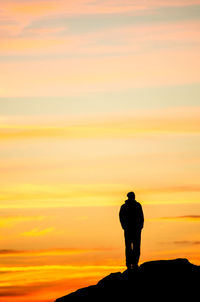 Silhouette man standing on rock against orange sky